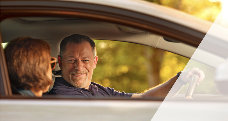 A man in the driver’s seat looks at a woman in the passenger seat as they sit in a car together.