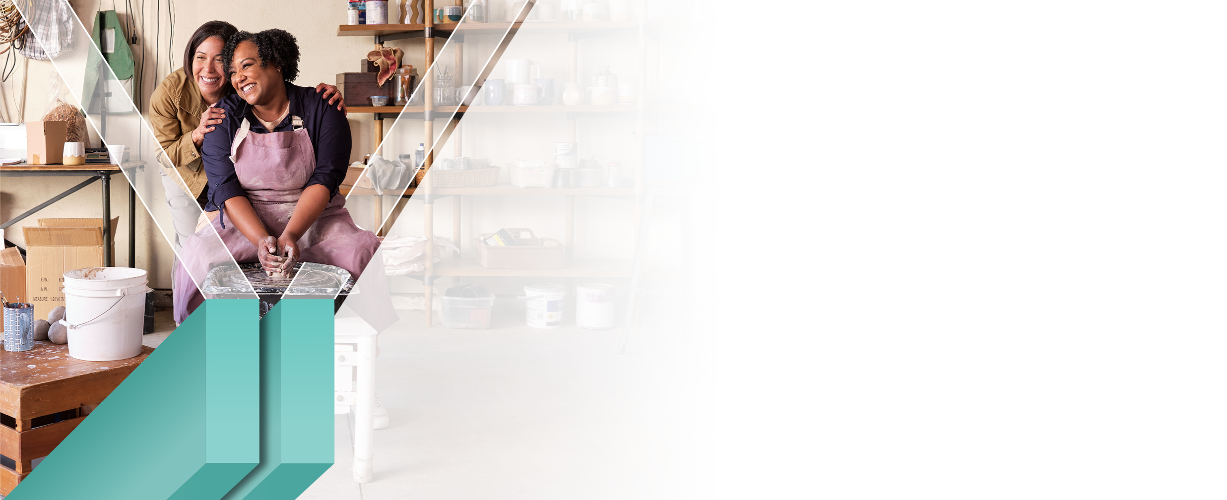 A woman happily makes pottery as her friend stands behind her giving an encouraging hug.